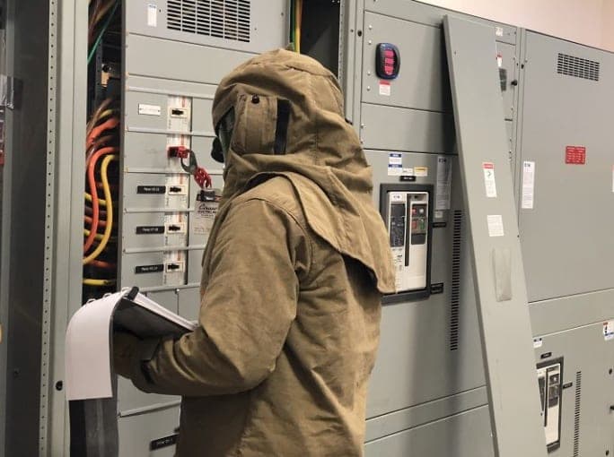 A PowerSafe engineer in arc-rated PPE collecting field data at open, energized switchgear
