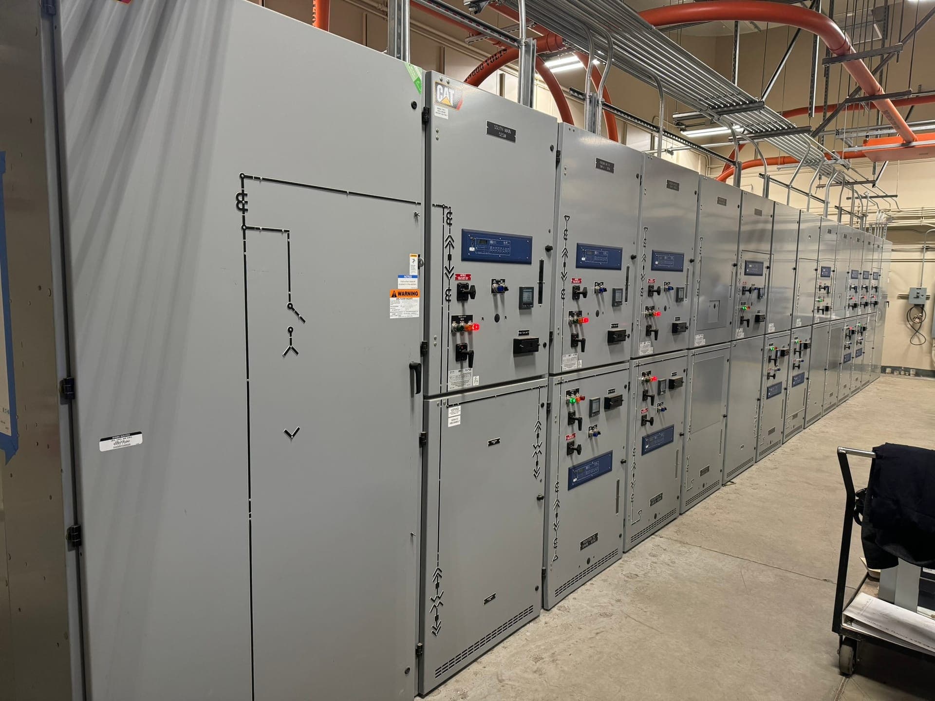 Medium-voltage switchgear lineup with an NFPA 70E arc flash warning label applied, in a facility electrical room